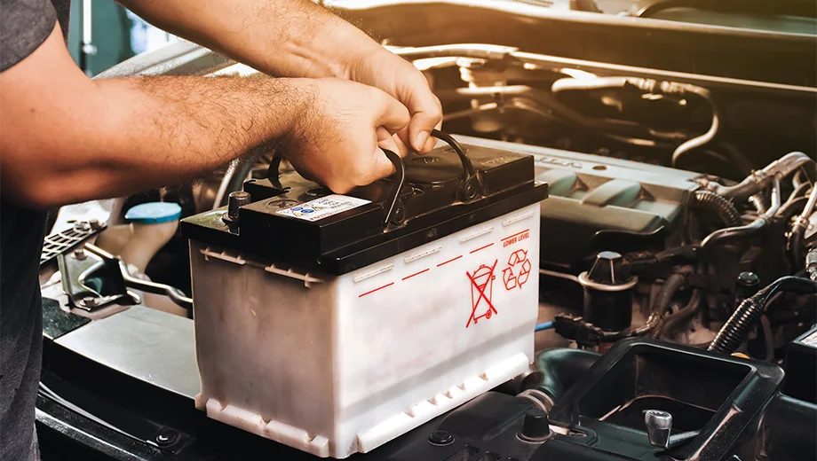 Man removes a car battery, demonstrating the process of determining battery replacement frequency.