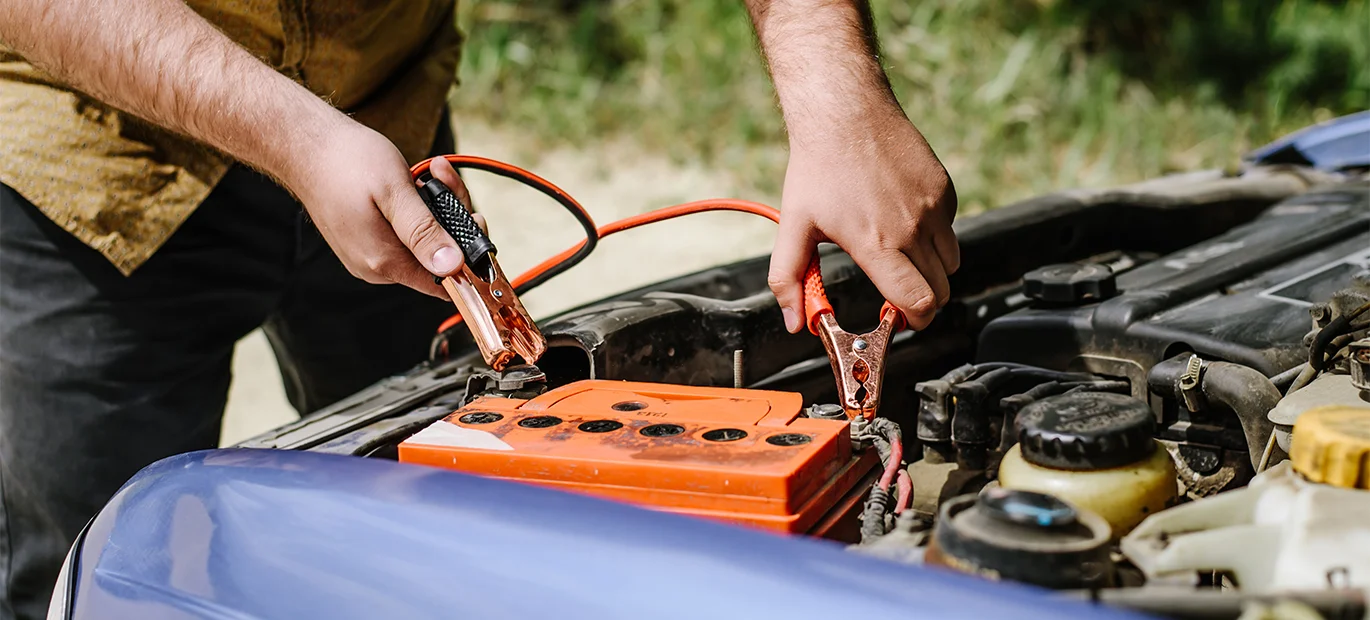 A man attaching a pair of jump leads to a car battery while demonstrating how to jump-start a car.