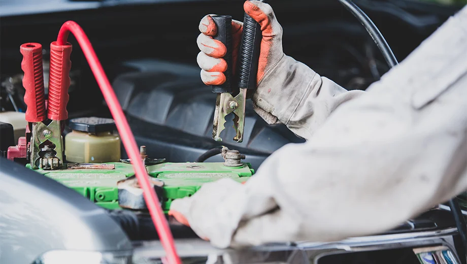 A man attaching a pair of jump leads to a car battery while demonstrating the step-by-step guide to effective jump-starting.