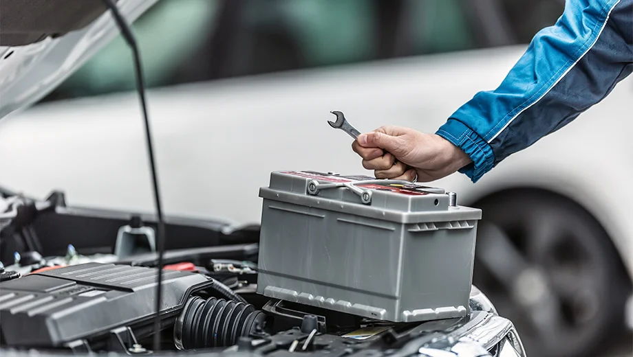 A man holding tools while inspecting a car battery, demonstrating tips for car battery maintenance.