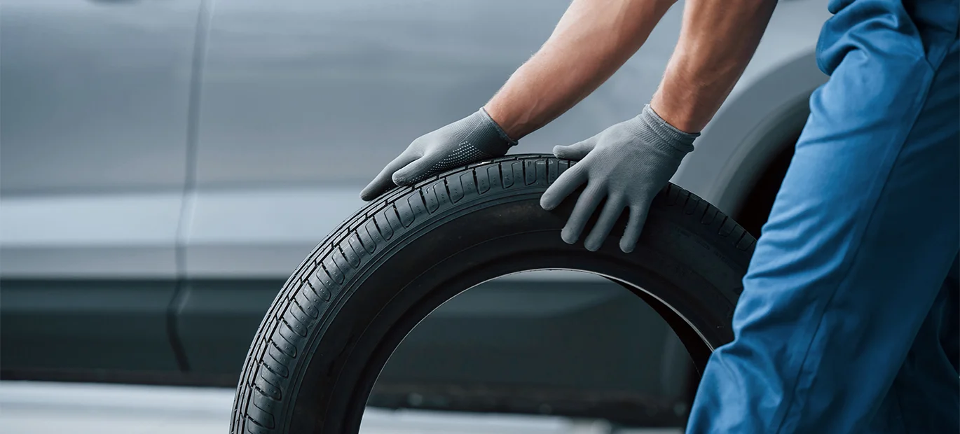 Mechanic rolling tyre signifies maintenance. Learn when to change car tyres for safe driving and optimal performance.