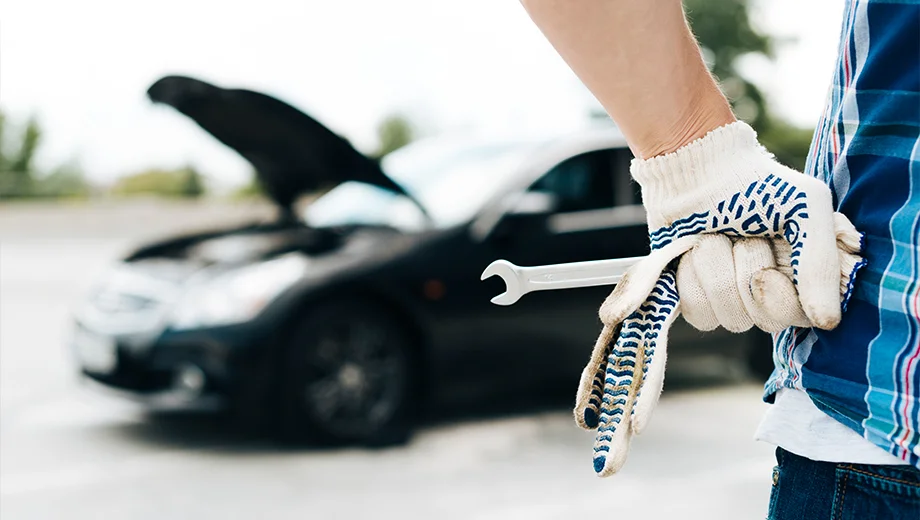 Man holding tools and inspecting a car with the hood open.