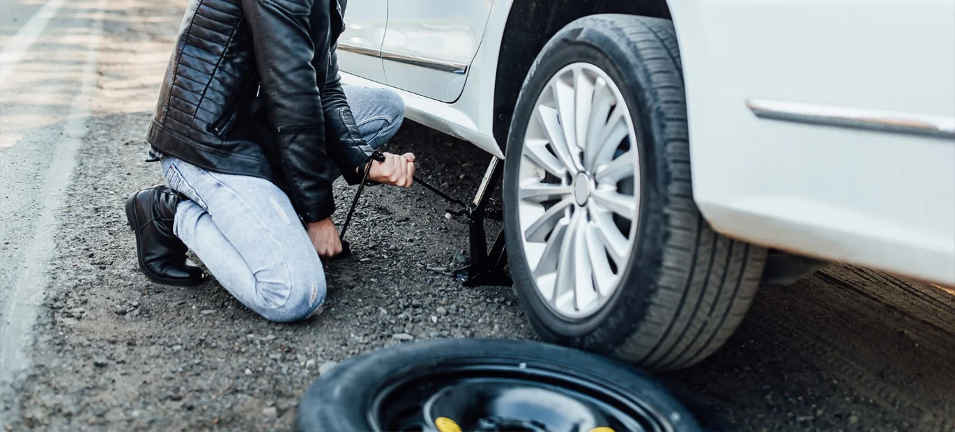 A man attempting to change a tyre in his car.