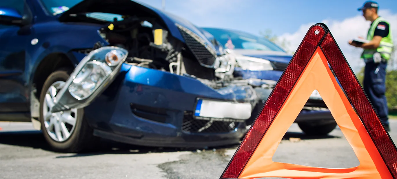 Two cars were involved in a crash on the road, with a safety triangle in the foreground and a person in the background documenting the accident.