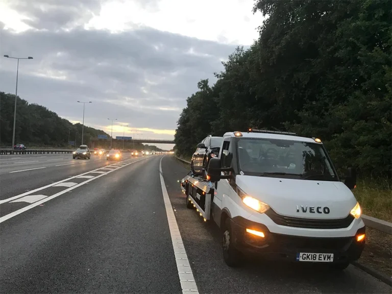 White tow truck providing 24/7 vehicle recovery on a major London highway during dusk.