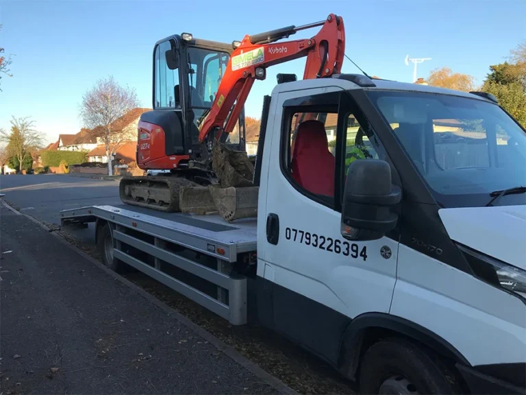 Vehicle recovery and machinery transport in Edgware: White truck carrying an orange excavator on a residential street.
